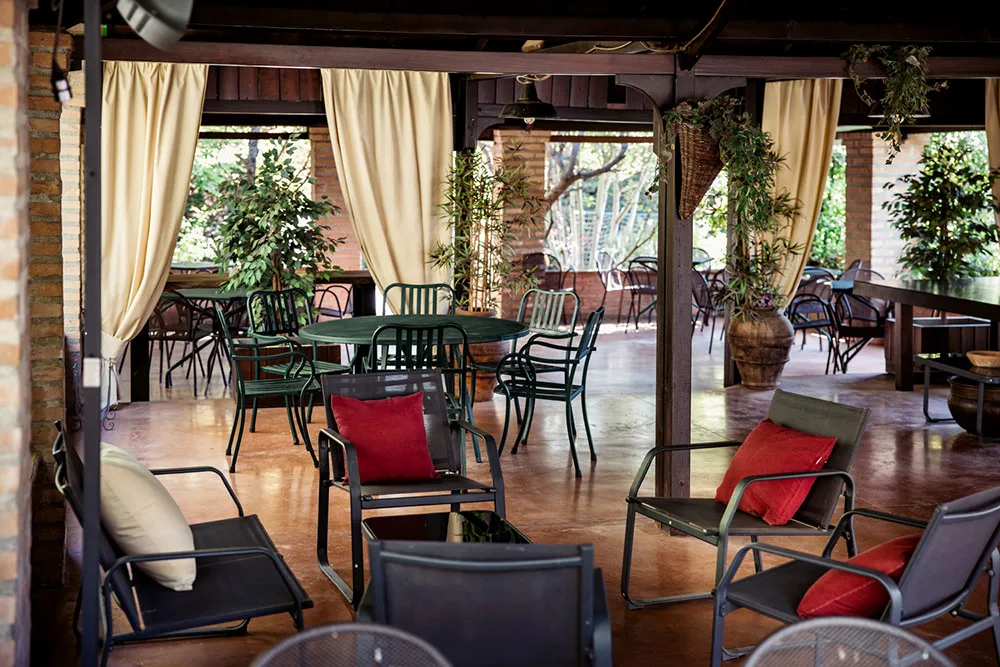 Area lounge coperta con tavoli, poltrone e cuscini rossi tra piante verdi