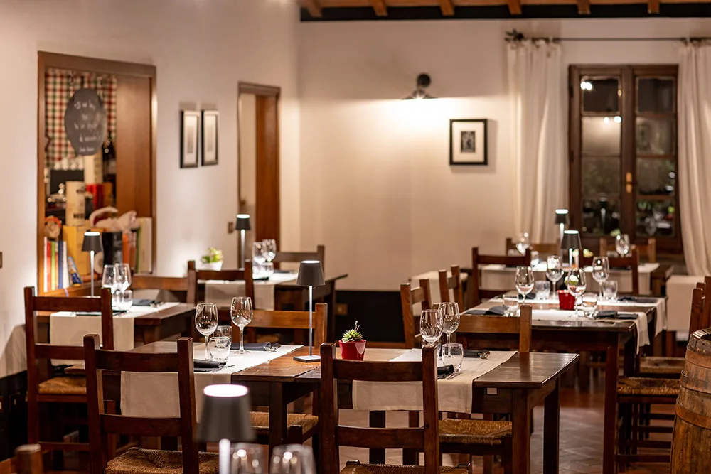Sala ristorante interna con tavoli in legno apparecchiati e lampade da tavolo