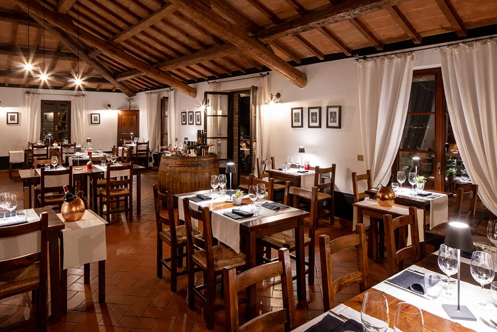 Ristorante rustico serale con travi in legno, botti e tavoli apparecchiati