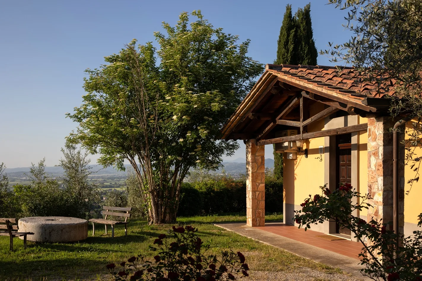 Portico di casetta gialla con vista sulla campagna e roseto in giardino