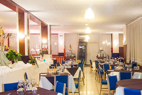Sala ristorante con tavoli rotondi apparecchiati, sedie blu e illuminazione soffusa