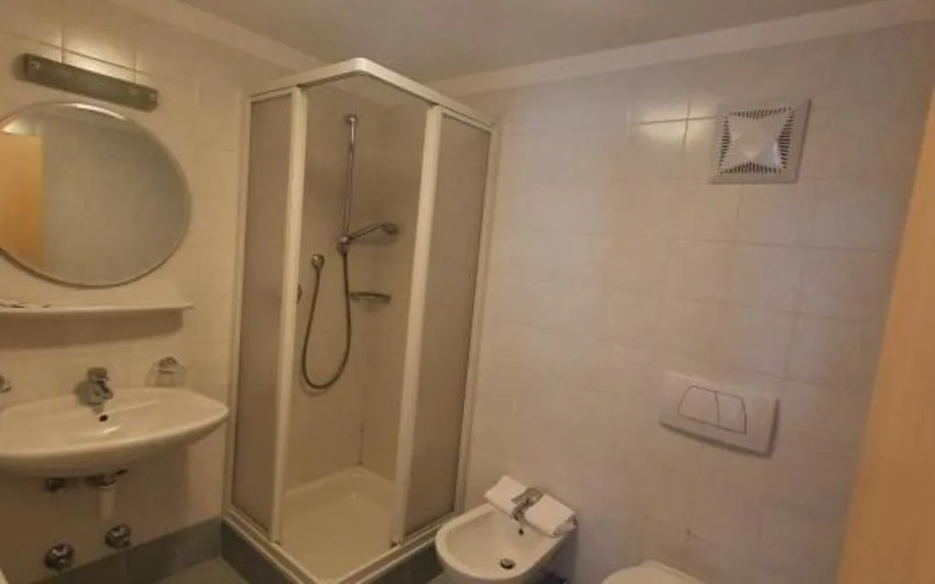 Bagno con doccia angolare, lavabo con specchio tondo e bidet