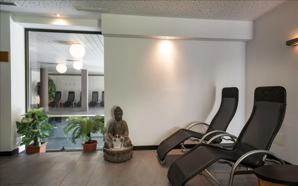 Zona relax con lettini neri, statua di Buddha e vista sulla piscina interna