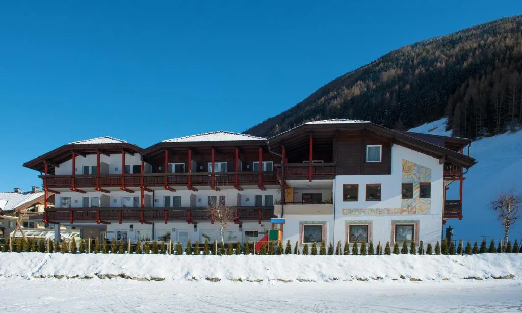 Facciata dell'hotel alpino con balconi in legno e affreschi, circondato dalla neve