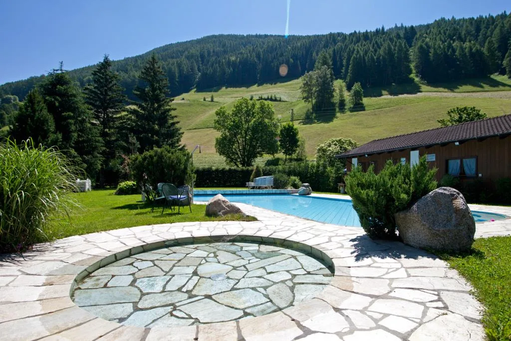 Giardino con piscina esterna e vasca idromassaggio circolare in pietra tra prati e boschi