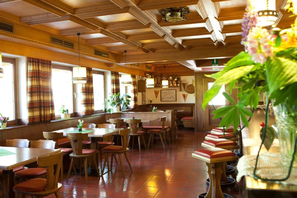 Sala ristorante rustica con soffitto in legno, tavoli e sedute in stile tirolese