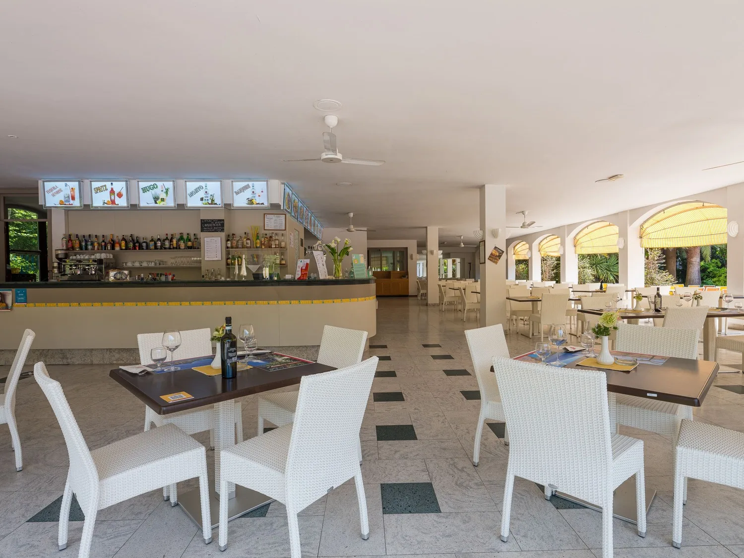 Area bar e ristorante interna con tavoli, sedie bianche e bancone con bottiglie