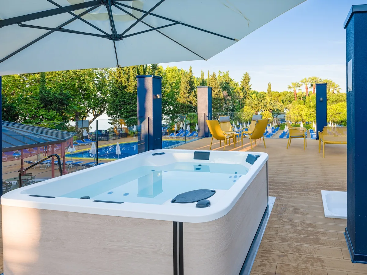 Vasca idromassaggio esterna su terrazza in legno con ombrellone e poltrone gialle