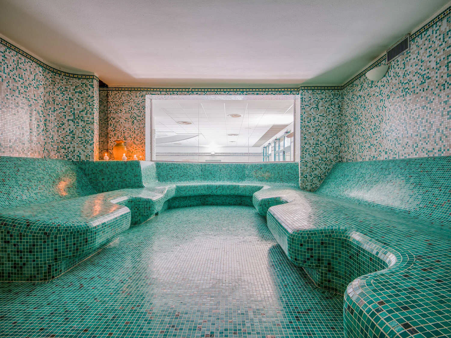 Bagno turco con panche curve rivestite di mosaico verde e grande finestra