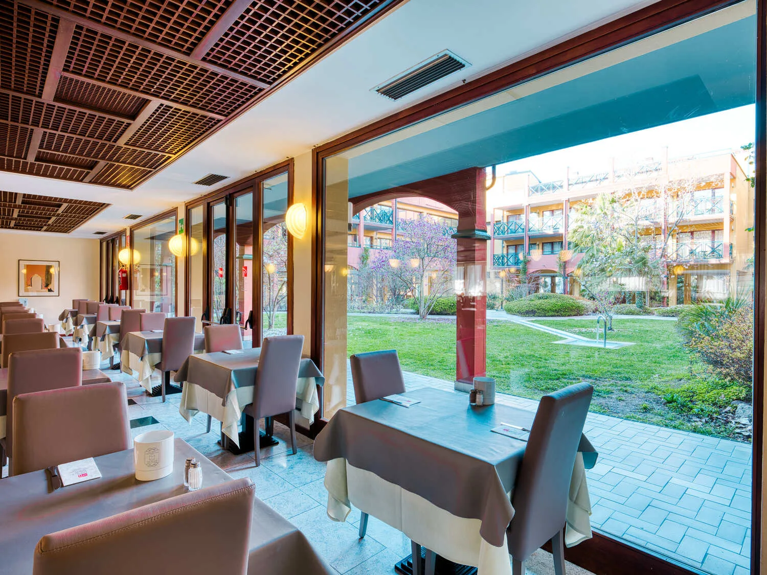 Sala ristorante con tavoli apparecchiati e ampie vetrate affacciate sul giardino