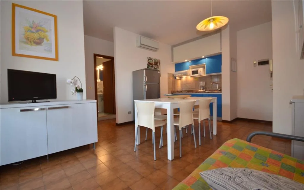 Zona giorno con cucina blu, frigorifero e tavolo da pranzo bianco