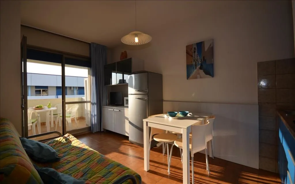 Soggiorno con divano colorato, tavolo e accesso al balcone soleggiato