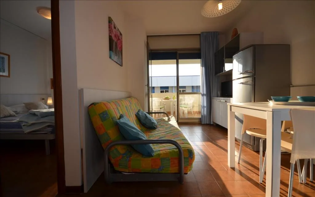 Zona giorno con divano letto colorato, cucina e camera vista