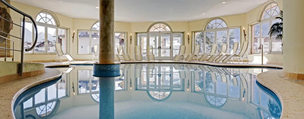 Piscina coperta con lettini e grandi finestre ad arco con vista sulla neve