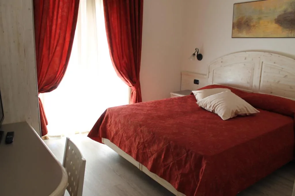 Camera matrimoniale con copriletto rosso e tende rosse alla finestra