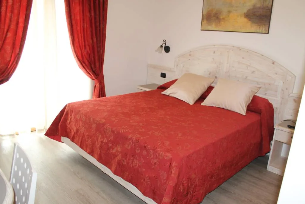 Camera doppia con copriletto rosso, tende rosse e testiera in legno chiaro