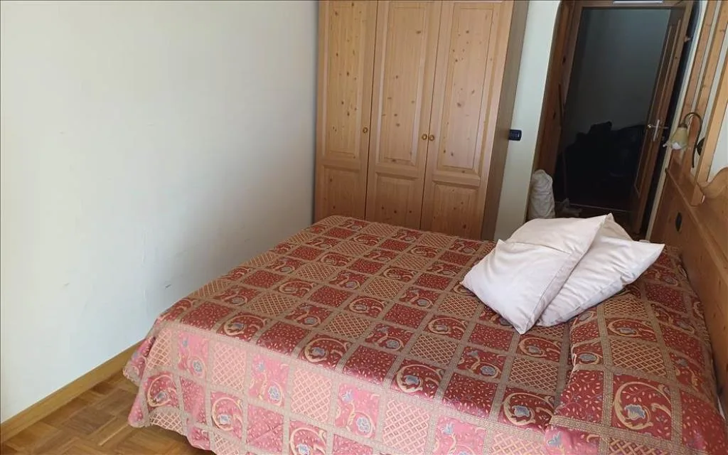 Camera semplice con letto, copriletto decorato e armadio in legno