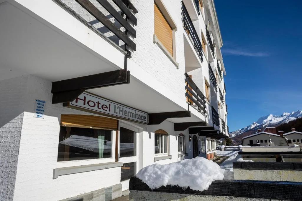 Ingresso dell'Hotel L'Hermitage con insegna e montagne innevate