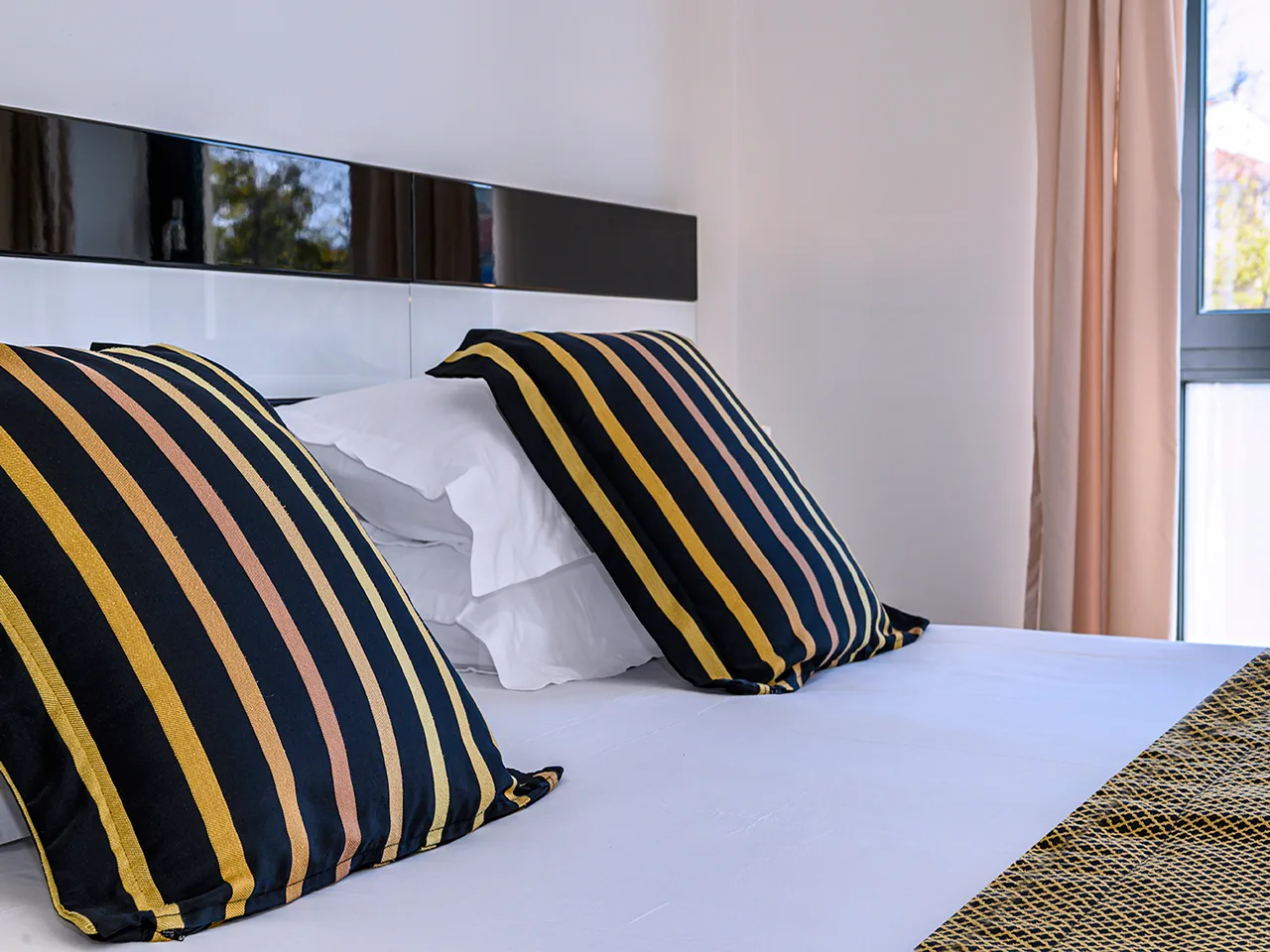 Dettaglio di letto con cuscini a righe blu e gialle e testiera moderna