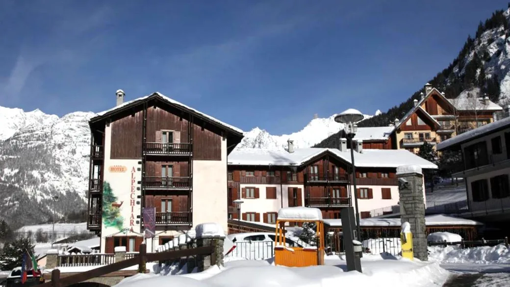 Esterno dell'Hotel Alpechiara con cumuli di neve e montagne innevate sullo sfondo
