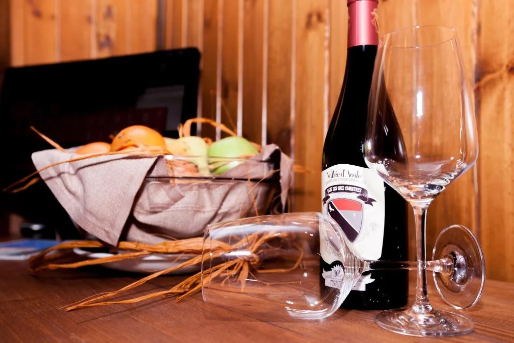 Bottiglia di vino rosso Valle d'Aosta con bicchieri e cesto di frutta su tavolo in legno