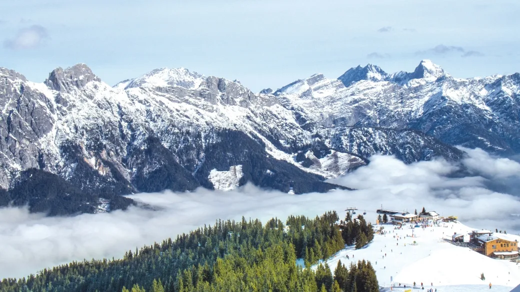 Vista panoramica delle cime innevate con foresta e comprensorio sciistico tra le nuvole
