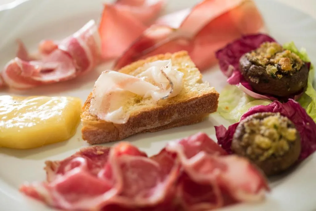 Antipasto di salumi affettati con crostino, formaggio e funghi ripieni su piatto bianco