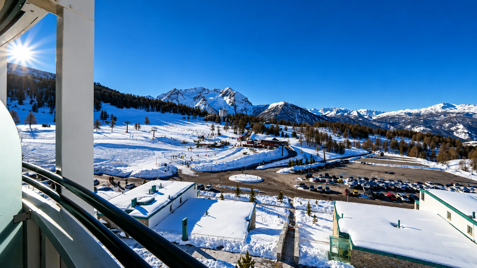 Vista dal balcone dell'hotel su piste da sci, montagne innevate e cielo azzurro