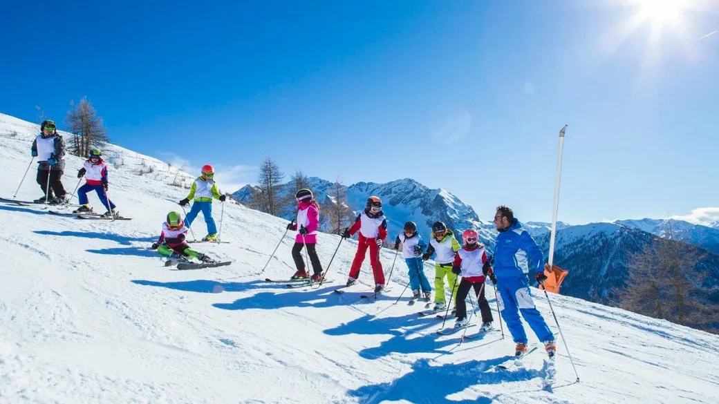 Lezione di sci con maestro e gruppo di bambini su pista innevata in giornata di sole