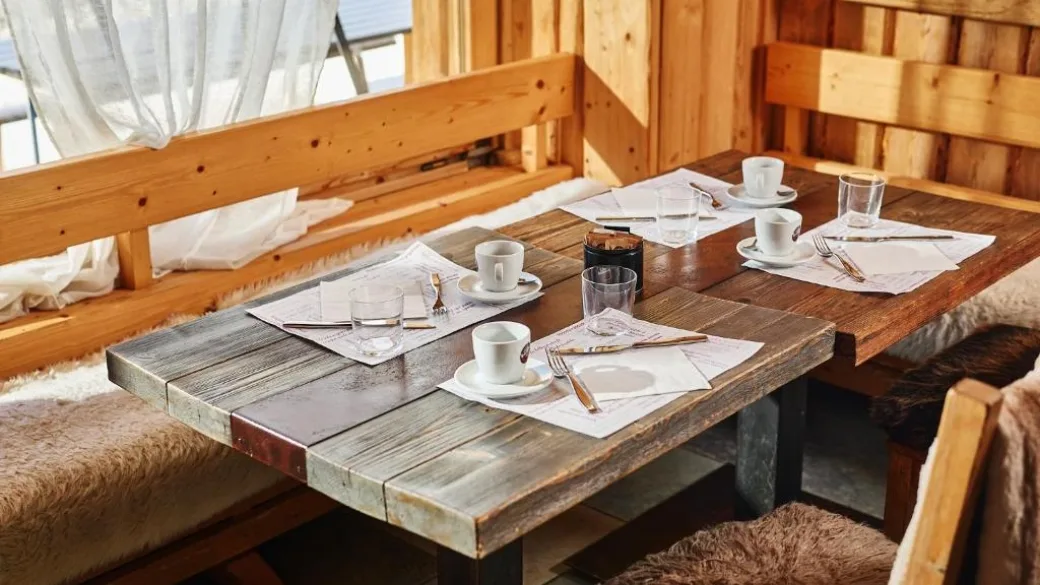 Tavolo in legno apparecchiato per la colazione con tazze e panche rivestite di pelliccia