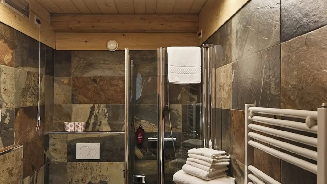 Bagno con doccia in vetro, piastrelle in pietra e asciugamani bianchi