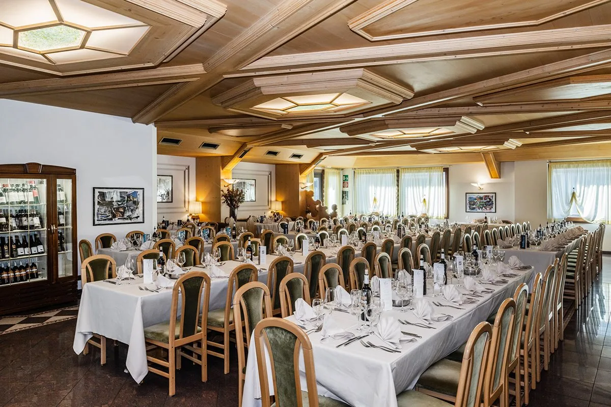 Sala ristorante allestita con tavoli lunghi e soffitto in legno decorato