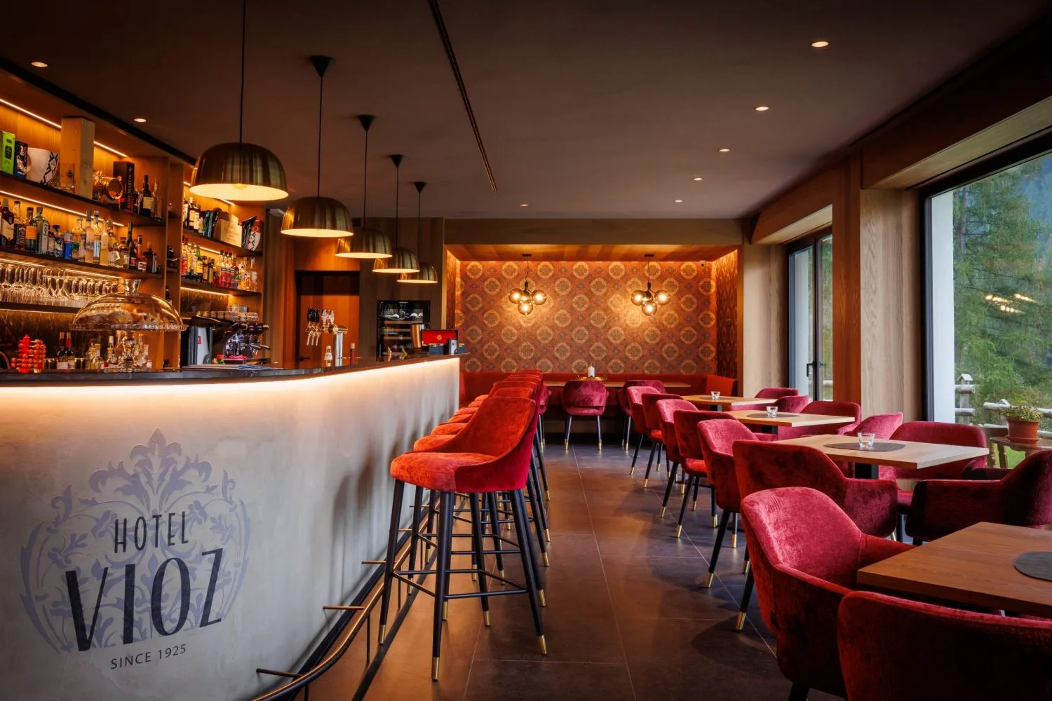 Bar dell'Hotel Vioz con sgabelli rossi, bancone illuminato e tavoli