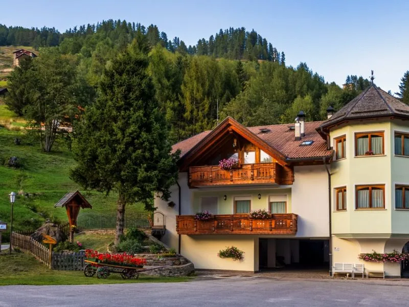 Casa alpina con balconi in legno fioriti circondata dal verde