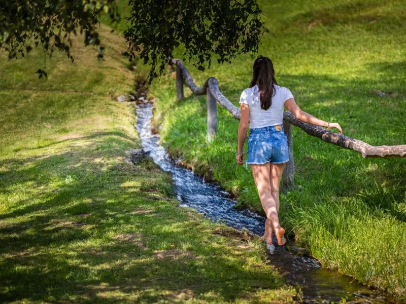 Donna che cammina lungo un ruscello in un prato verde alpino