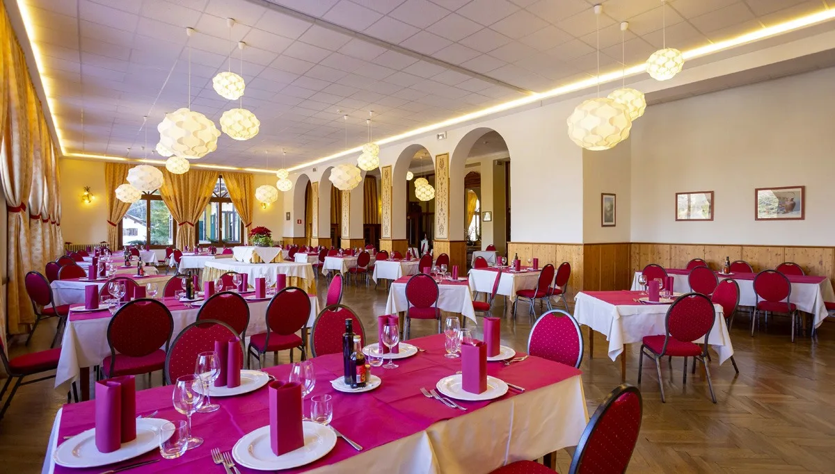 Ampia sala ristorante con tavoli apparecchiati, sedie rosse e lampadari sferici