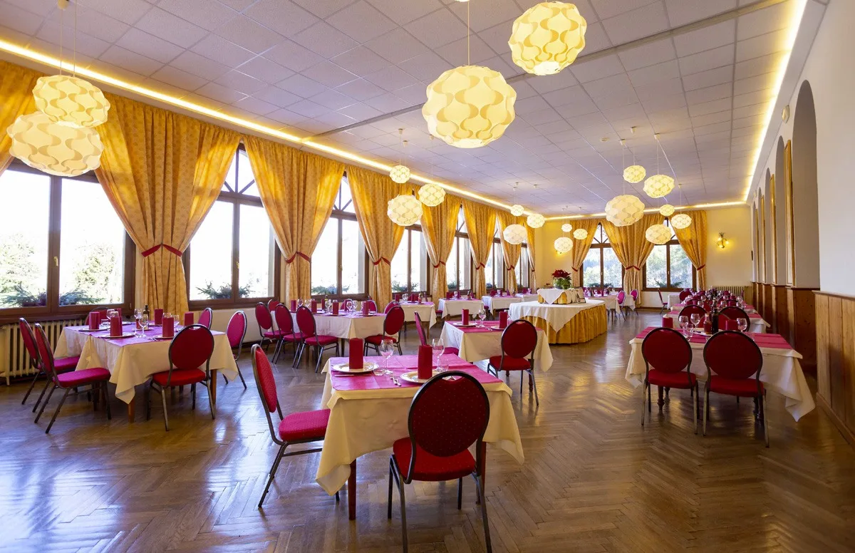 Sala da pranzo luminosa con grandi finestre, tende dorate e tavoli eleganti
