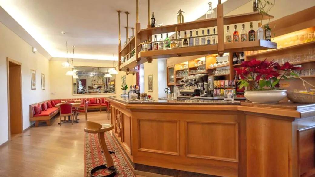 Bar interno dell'hotel con bancone in legno, sgabelli e angolo salotto con divani rossi