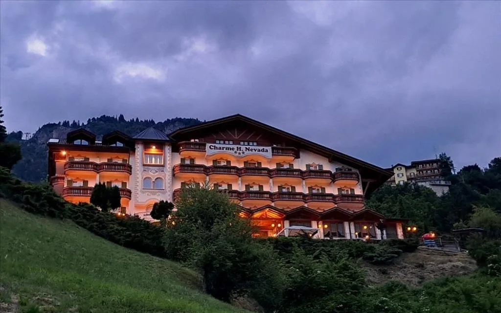 Facciata illuminata del Charme Hotel Nevada al tramonto su una collina verde