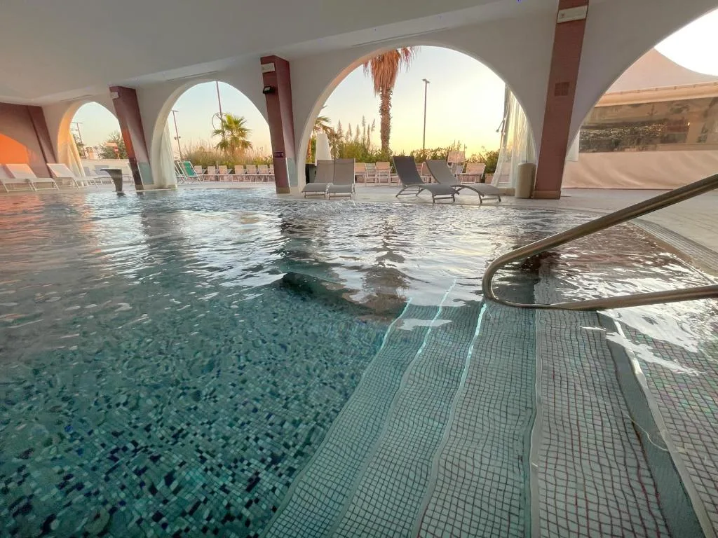 Piscina con archi affacciata sul tramonto e lettini sul bordo