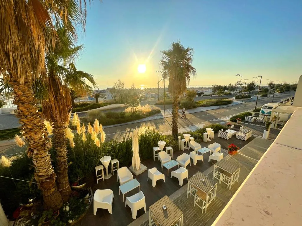 Terrazza esterna al tramonto con sedute bianche tra palme e vista mare