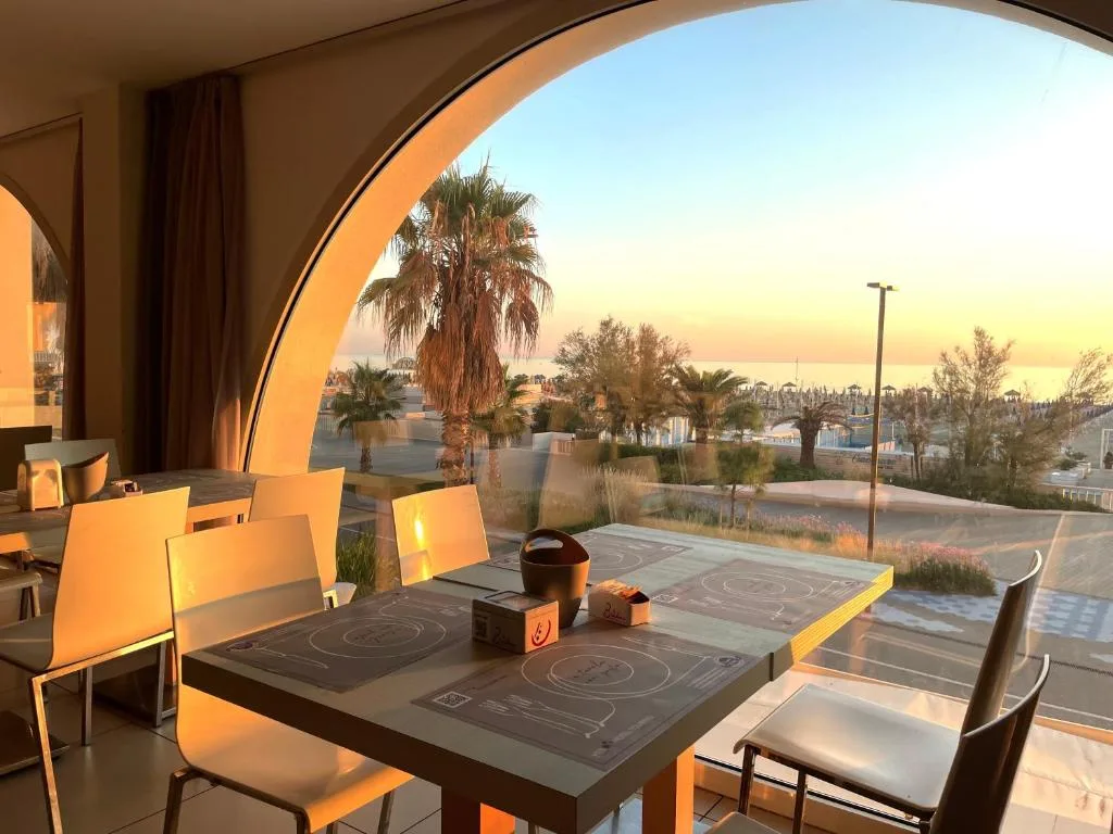 Tavolo del ristorante con grande finestra ad arco e vista tramonto sul mare