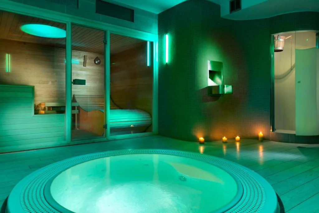 Zona spa con vasca idromassaggio e sauna illuminata di verde