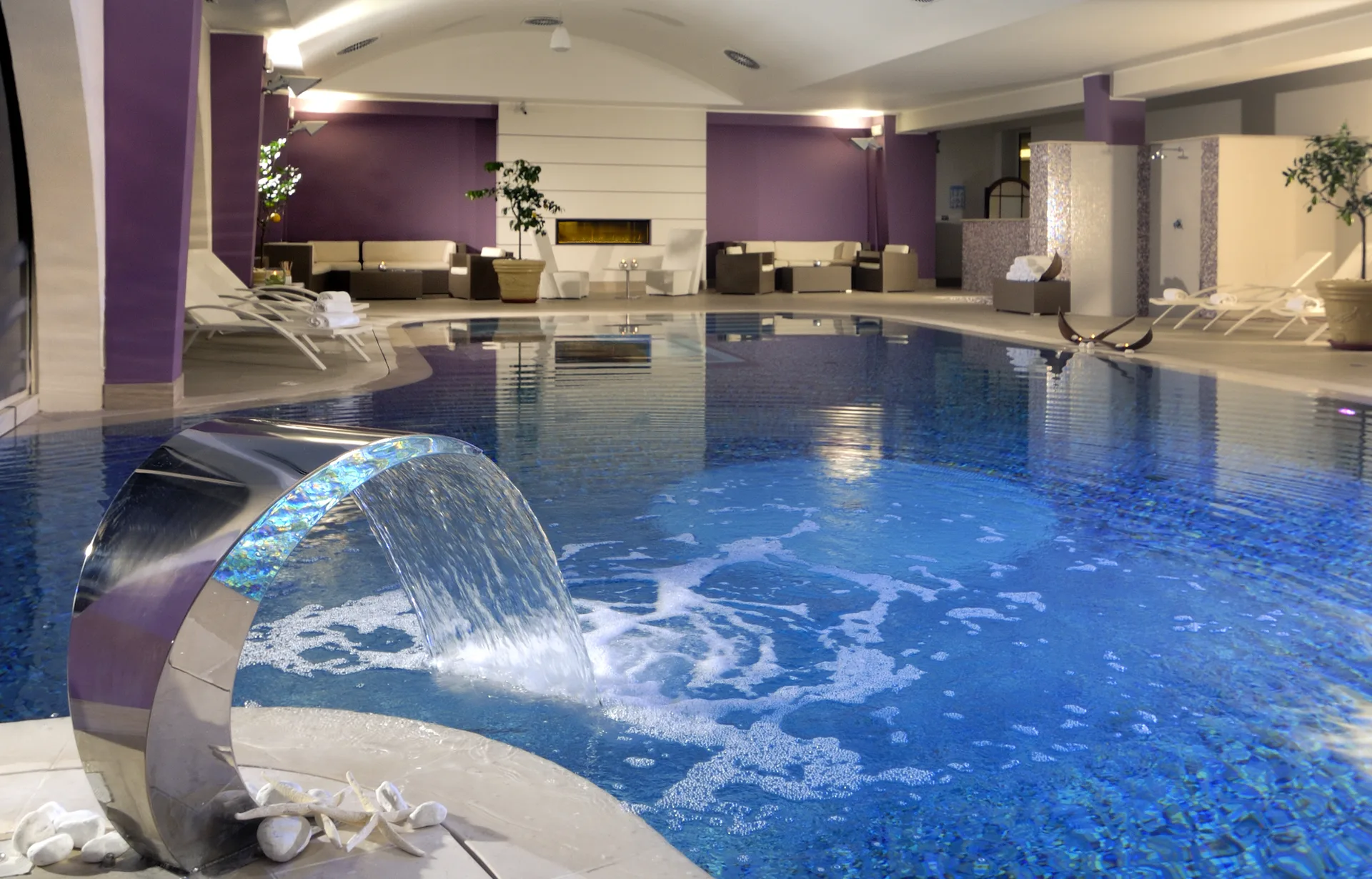 Piscina interna coperta con cascata e zona relax dai toni viola