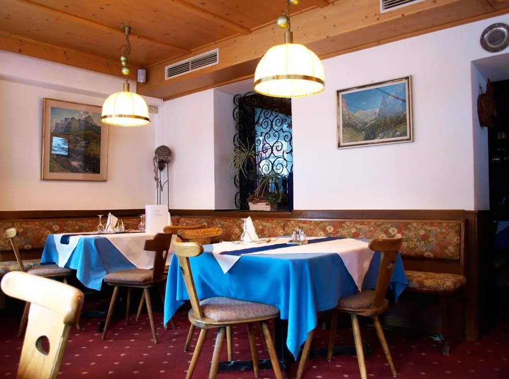 Sala ristorante con tavoli dai tovagliati azzurri e quadri di montagna alle pareti