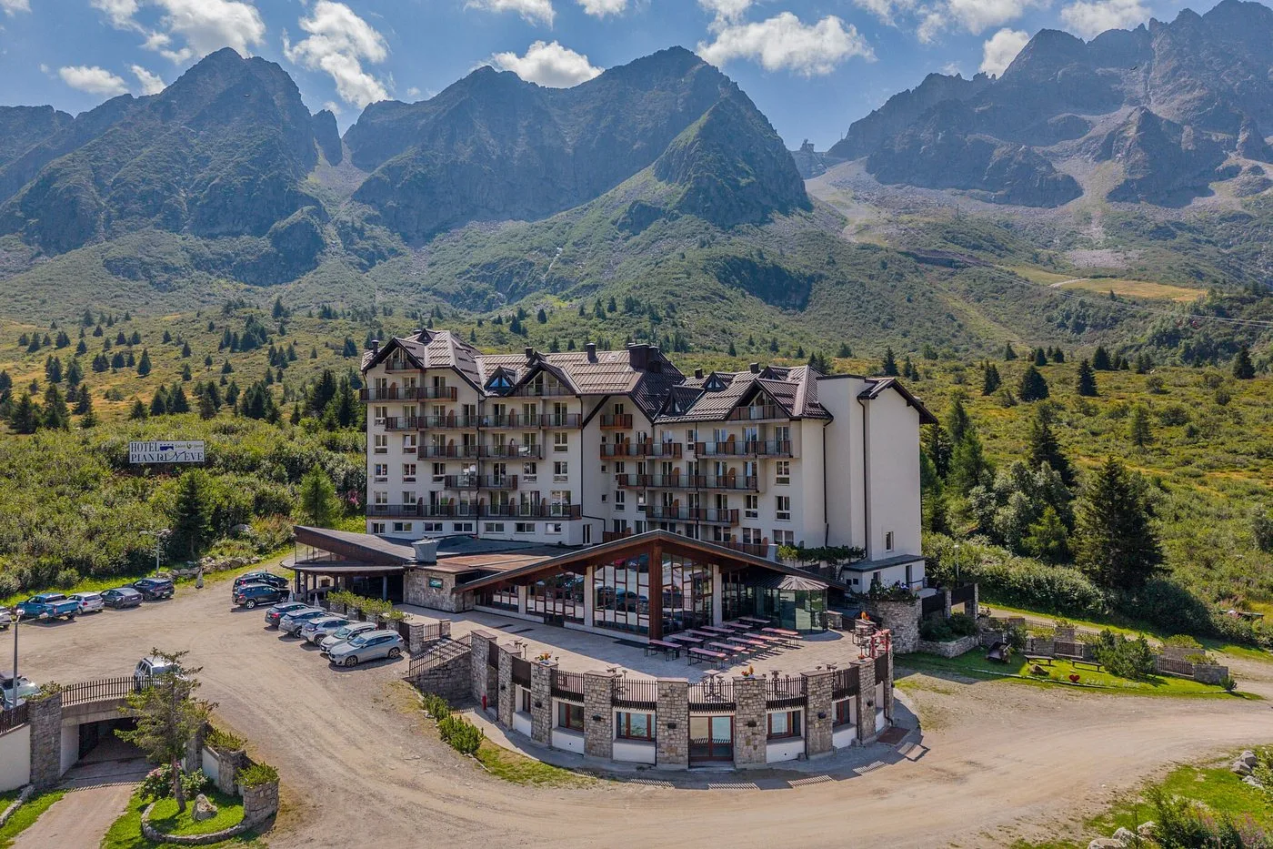 Veduta aerea estiva dell'hotel circondato da prati verdi e montagne rocciose