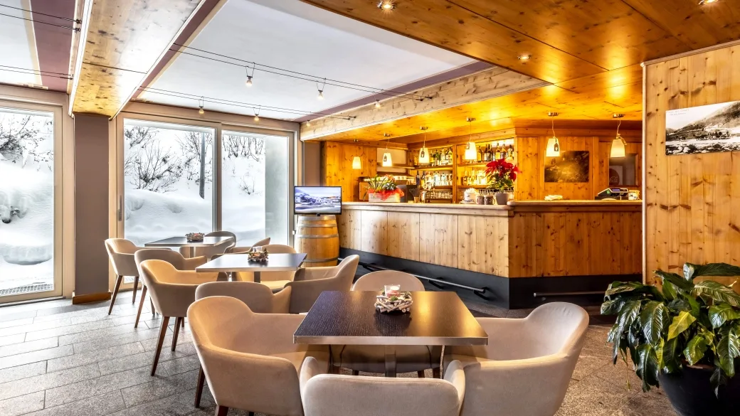 Area bar dell'hotel con tavolini, poltrone e vetrate affacciate sulla neve