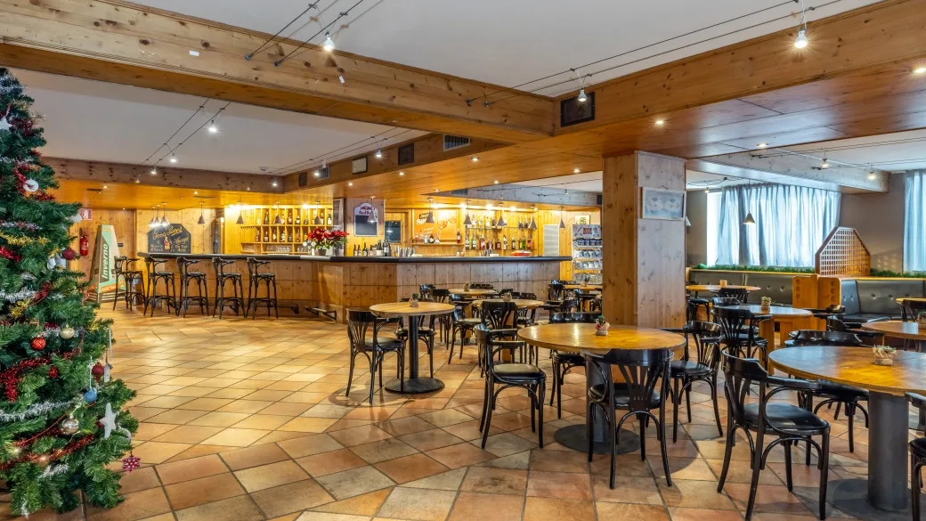 Sala comune con bar, tavoli, sedie e albero di Natale decorato