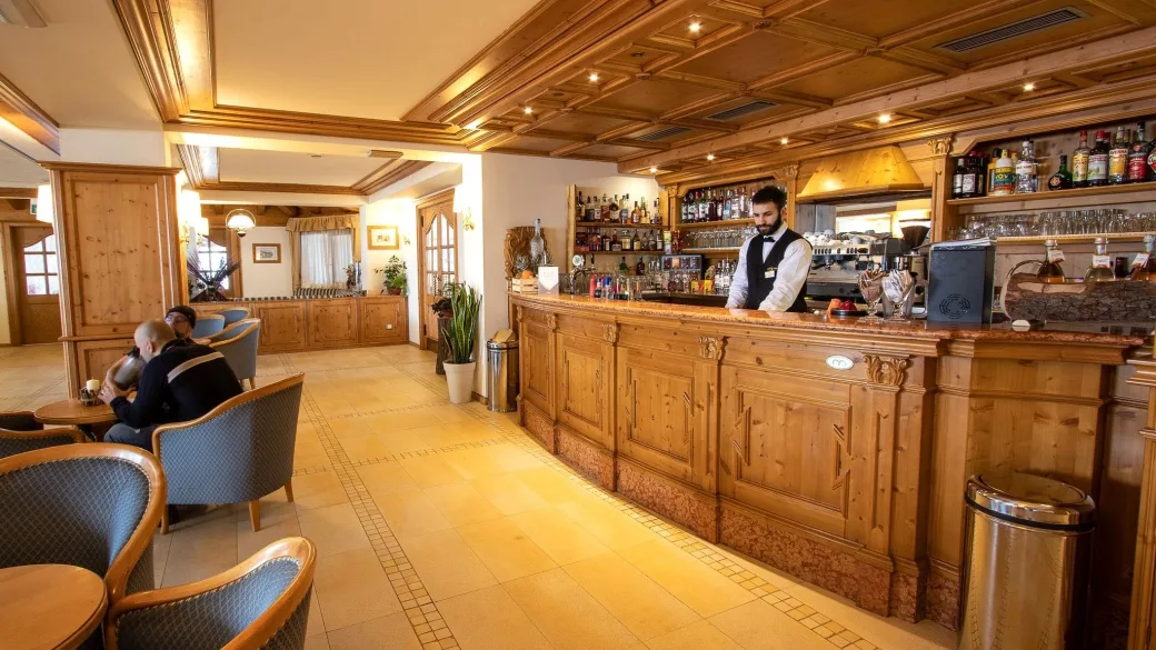 Bar dell'hotel con bancone in legno intagliato e barista al lavoro