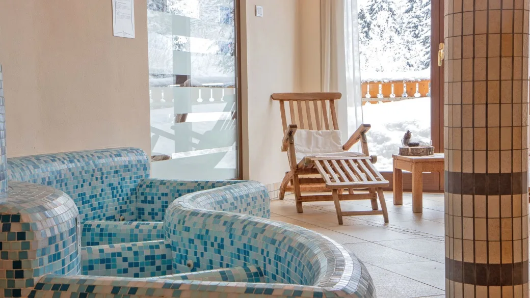 Area relax della spa con poltrone rivestite in mosaico azzurro e lettino in legno vicino alle vetrate